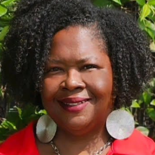 Dr Leah Raby is an African-American woman. She has shoulder-length black hair, and wearing large, round, disc-shaped ear rings.